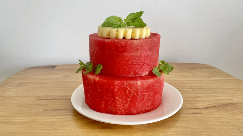 Two-tiered watermelon tower topped with pineapple and mint on wooden table