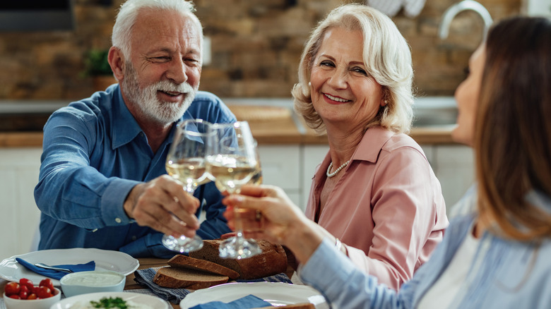 Older couple drinking toasting glasses with younger person
