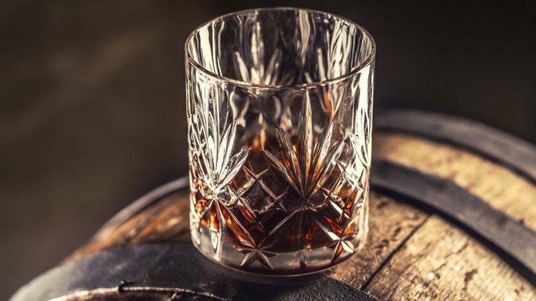 A glass of bourbon sitting atop an oak barrel.