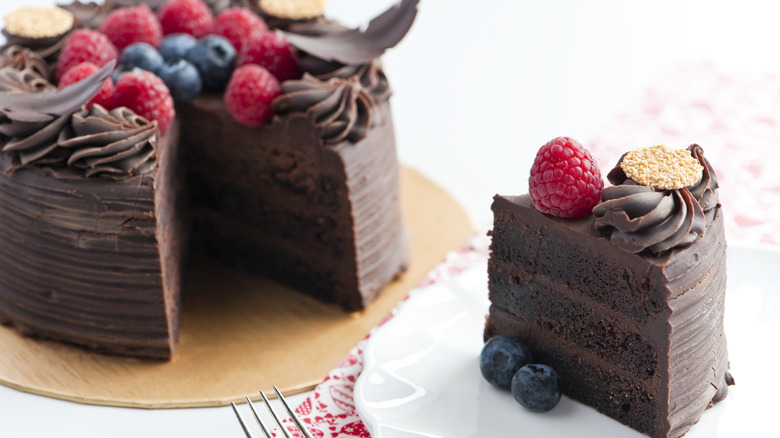 A layered chocolate cake with one slice separated from it and raspberries and blueberries on top