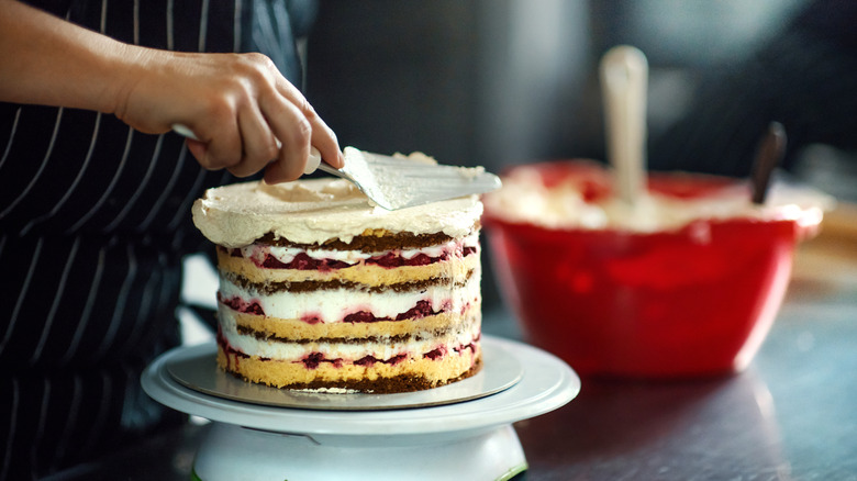 A baker frosting a layered cake while wearing an apron