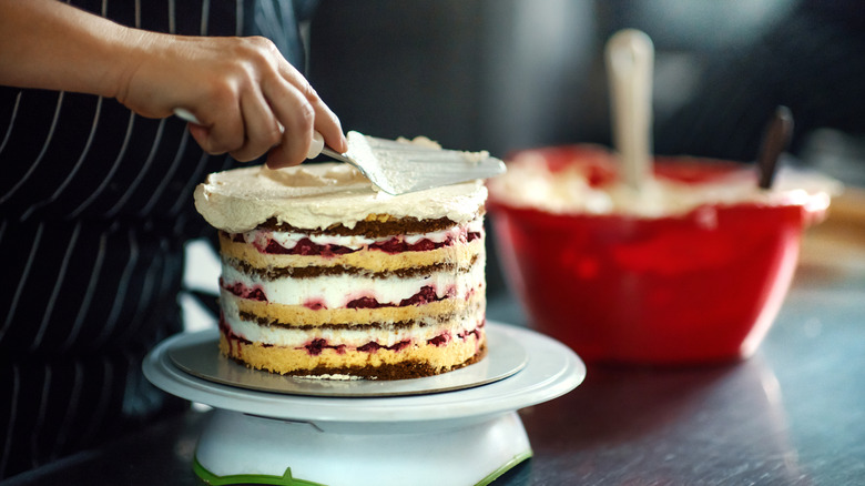 Person frosting a layered cake with white frosting