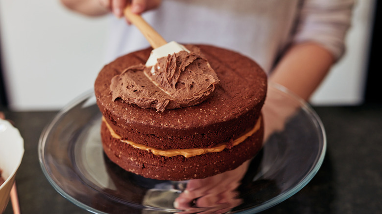 Rubber spatula spreading chocolate frosting on a chocolate layer cake