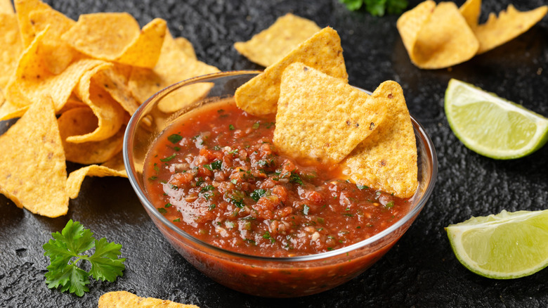 Mexican salsa roja with limes and chips on a table
