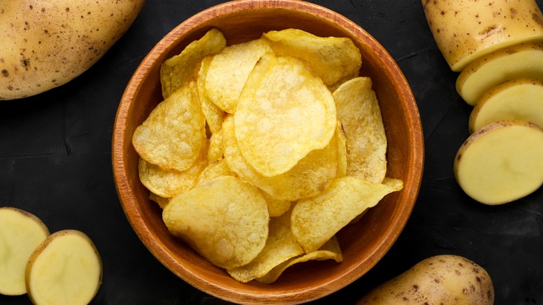 Potato chips in a bowl surrounded by raw potato slices