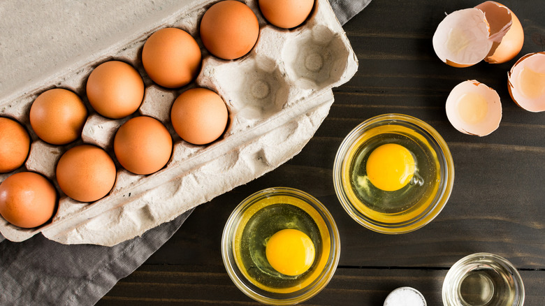 A carton of eggs with some cracked into small bowls