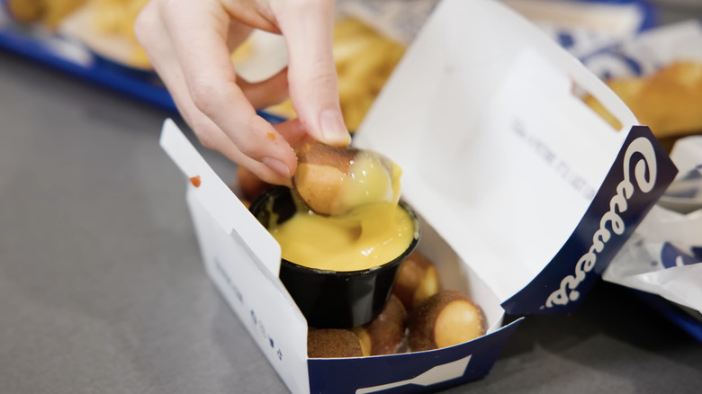 Hand dipping pretzel bite into Culver's cheese sauce.