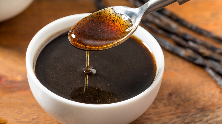 Spoon lifting vanilla bean paste out of small white bowl