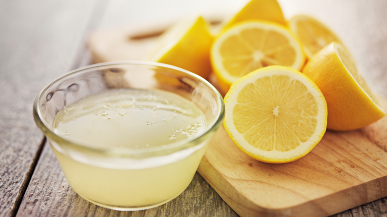 Sliced lemons next to a small glass bowl of fresh lemon juice.