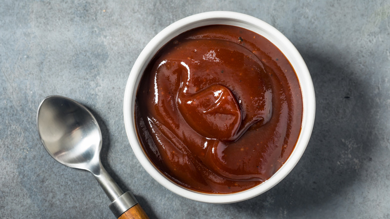 A small white ramekin full of homemade BBQ sauce with a silver spoon beside it