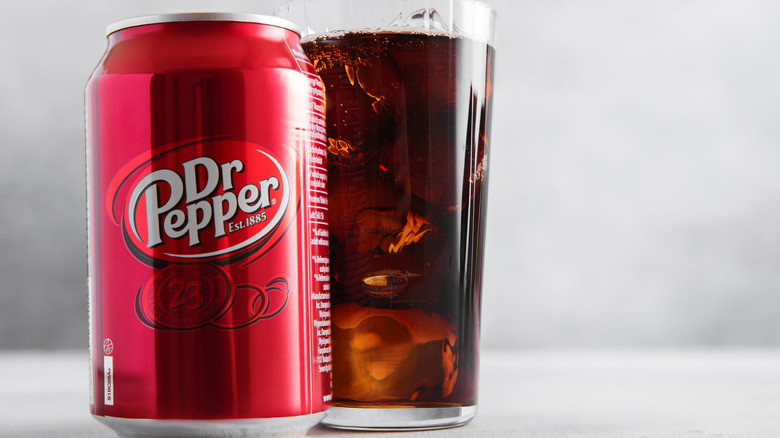 A can of Dr Pepper beside a glass full of the soda with ice in it.