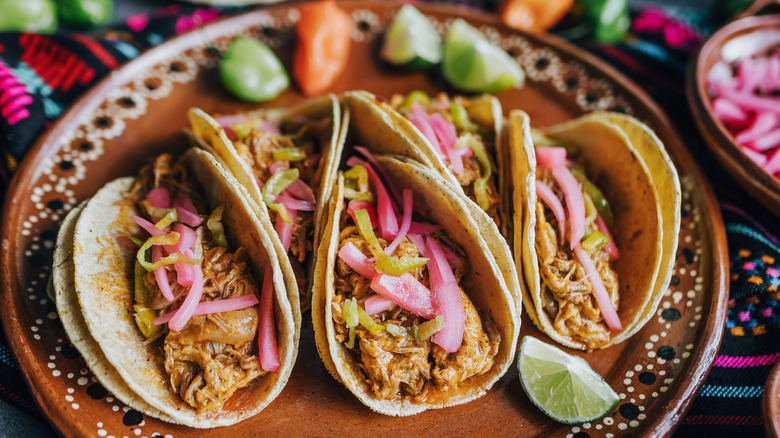 Plate of pork carnitas tacos with red onion and limes