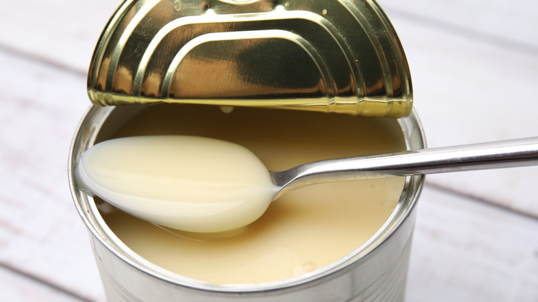 Open metal can of sweetened condensed milk with spoon