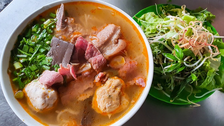 Bowl of brothy soup with various meats and herbs with bowl of greens
