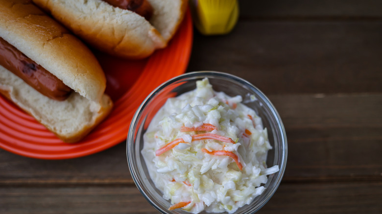 A bowl of coleslaw with hot dogs on a table
