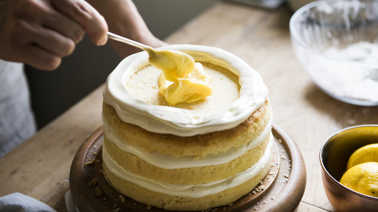 person decorating a layer cake with a plastic spoon