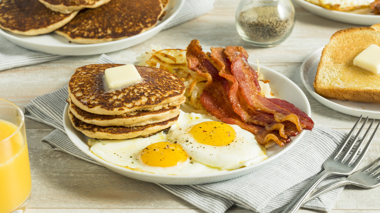 Fried eggs, bacon, hash browns, and pancakes on a plate with toast