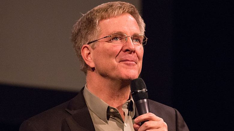 Rick Steves holds a microphone at a speaking event