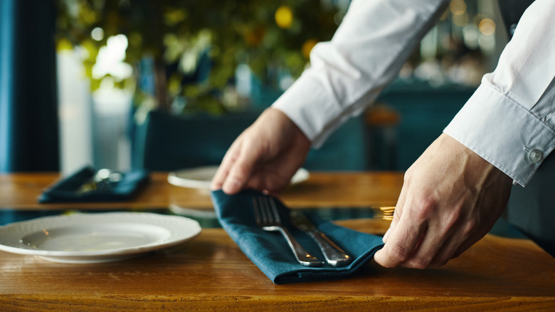 Hands place blue napkin with flatware on table