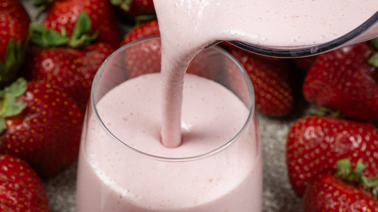 Close-up shot of thick strawberry smoothie being poured into glass from blender