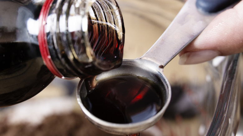 Close up of vanilla extract being poured into metal teaspoon