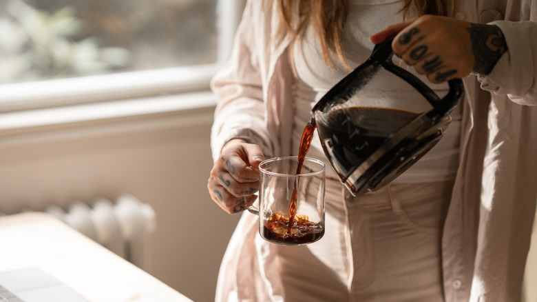 Woman pours pot of coffee into glass mug at home