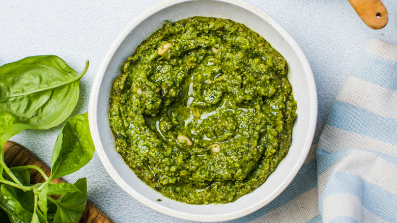 Green pesto in a white bowl with fresh basil leaves