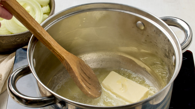 Butter being melted in a pot while stirring with a wooden spoon