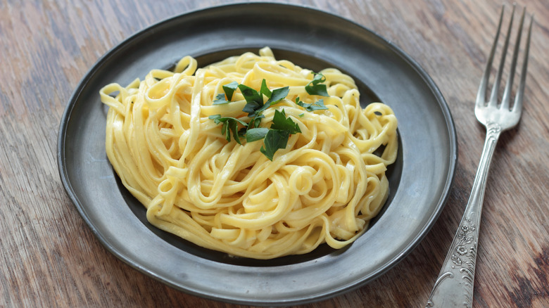 Buttered fettuccini in a black plate, topped with cut parsley