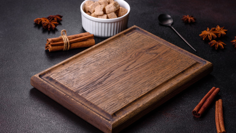 Sugar, cinnamon and other spices on a wooden cutting board on a dark concrete background.