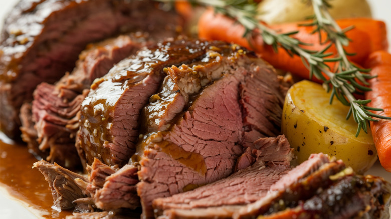 Sliced pot roast with gravy, potatoes, rosemary, and carrots