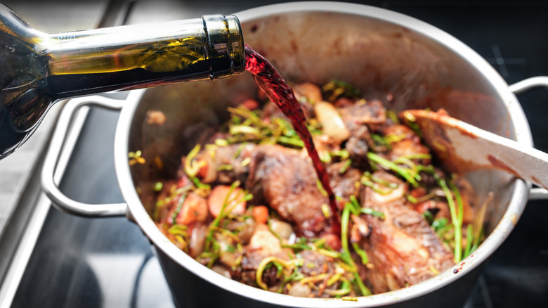 Pouring red wine into a pot of meat and veggies on a stove