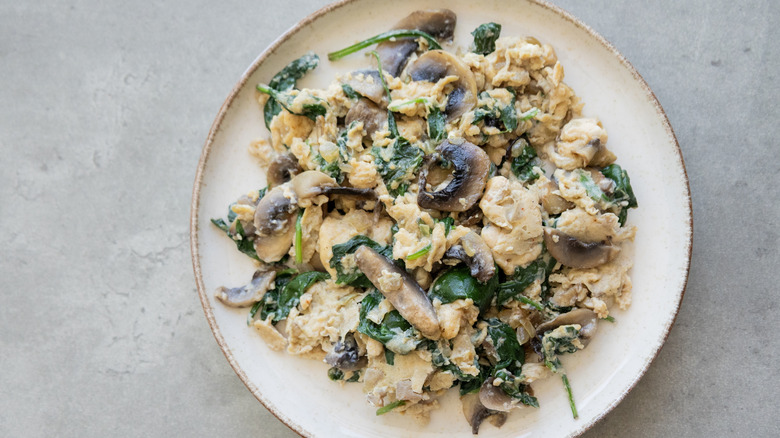Top view of a plate of scrambled eggs with spinach and mushrooms