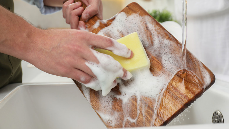 Hand washing a wooden cutting board with soap and sponge