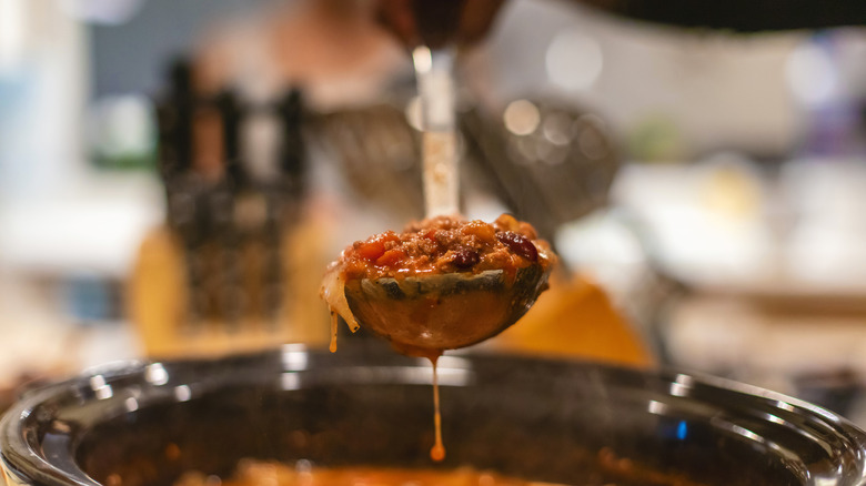 A ladle of chili hovering over a pot of stew