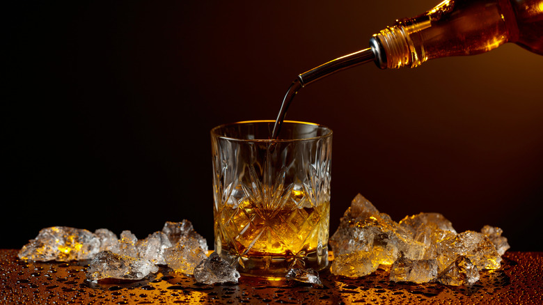Whiskey being poured into a glass beside melting pieces of ice