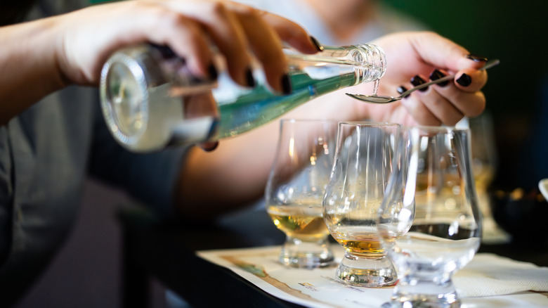 A person using a spoon to add water to glasses of whiskey