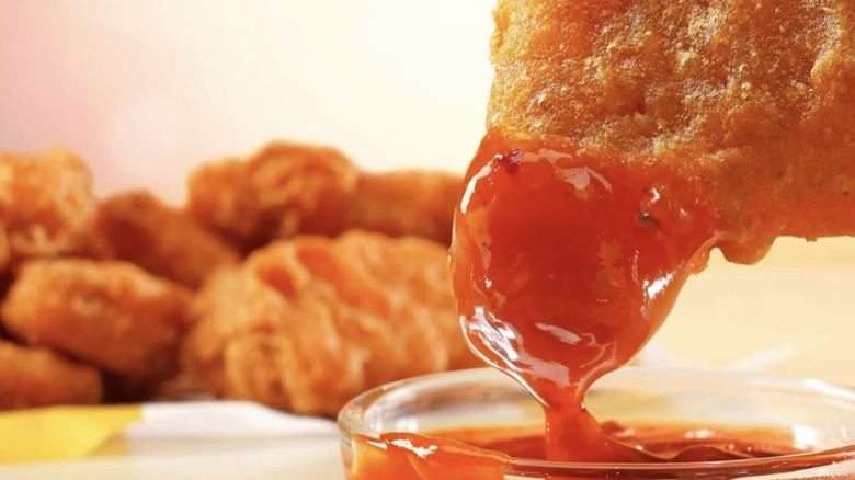 McDonald's McNugget being dipped into bright red sauce with flecks of chili pepper in it.