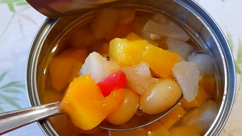 A closeup of an open canned fruit cocktail with a spoon inside holding fruit.