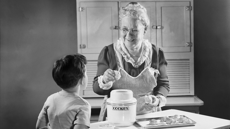A grandmother hands her grandson a cookie in a staged black and white photo.