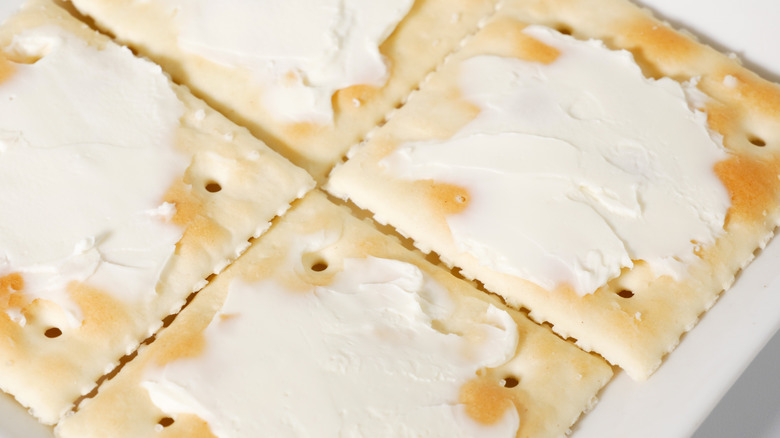 A closeup of saltine crackers with butter spread on top.