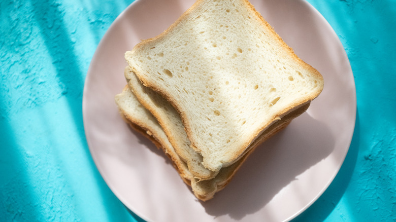 A stack of white bread sugar sandwiches on a plate sitting on a turquoise surface.