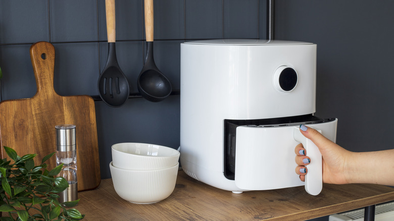 A hand opening a white air fryer on the kitchen counter.