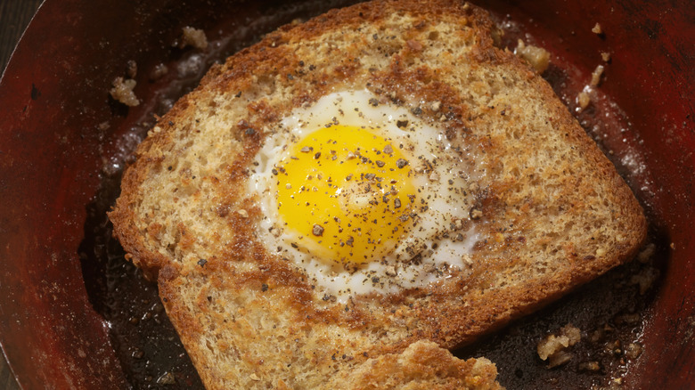 Sunny side up egg in a hole with bacon, topped with salt and pepper.