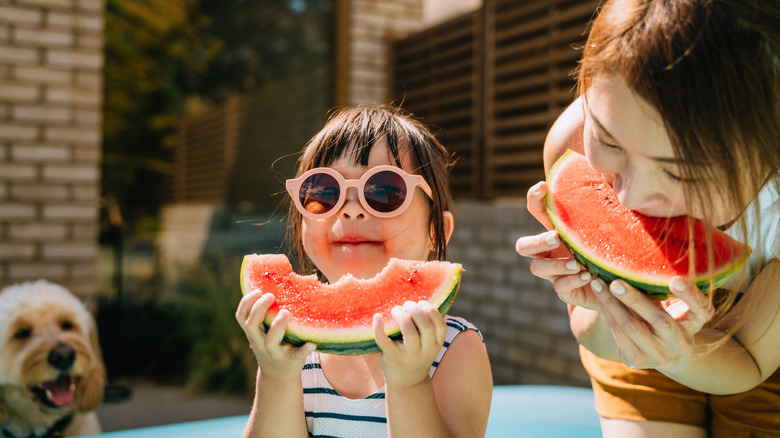 Little girl bites into a watermelon at the pool