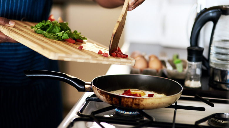 A person adds chopped vegetables to a pan on the stove