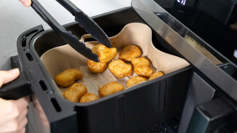 A person uses tongs to remove chicken nuggets from an air fryer