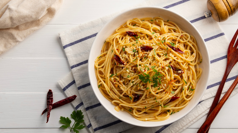 Homemade spaghetti aglio e olio with garlic, chili flakes, oil, fresh parsley and Parmesan cheese served in white plate.