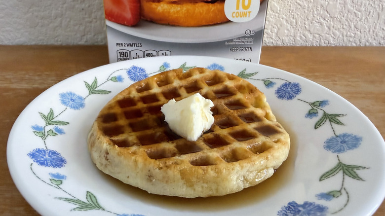 Aldi waffle on a small plate with syrup and butter, its box slightly visible in the background