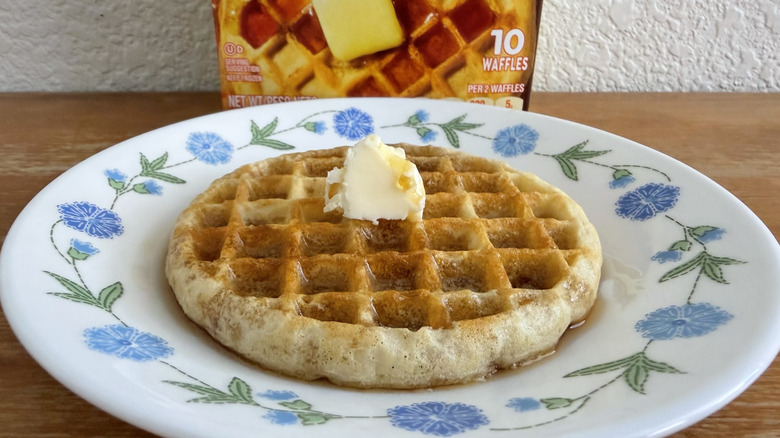 Eggo waffle on a small plate with syrup and butter, its box slightly visible in the background